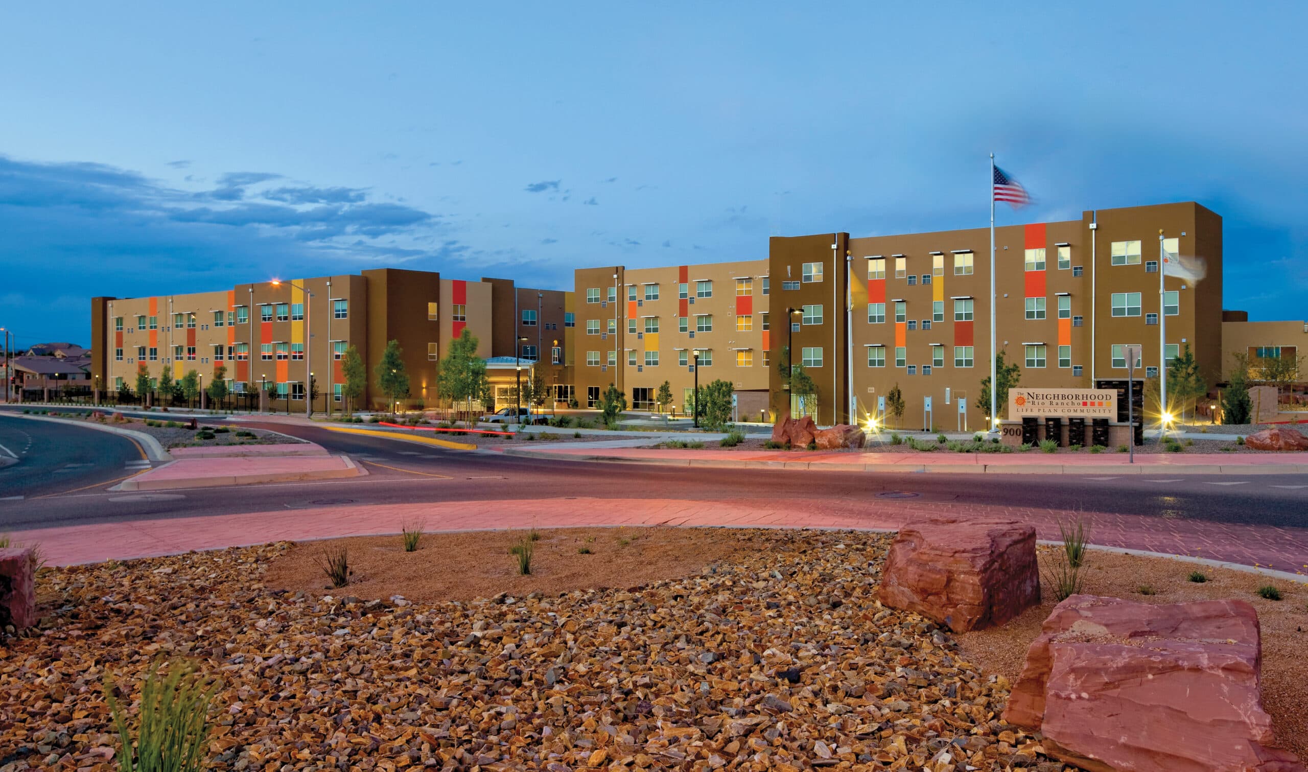 Modern multi-story community building at twilight with American flag and desert landscaping.
